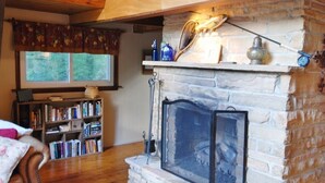 Un salon chaleureux avec une cheminée en pierre, une bibliothèque et une fenêtre avec des rideaux.