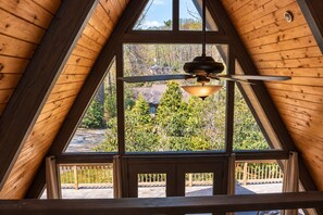 A room with a sloped ceiling, large windows, and a ceiling fan.