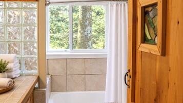 Un baño con bañera, ventana con vistas al follaje y puerta de madera.