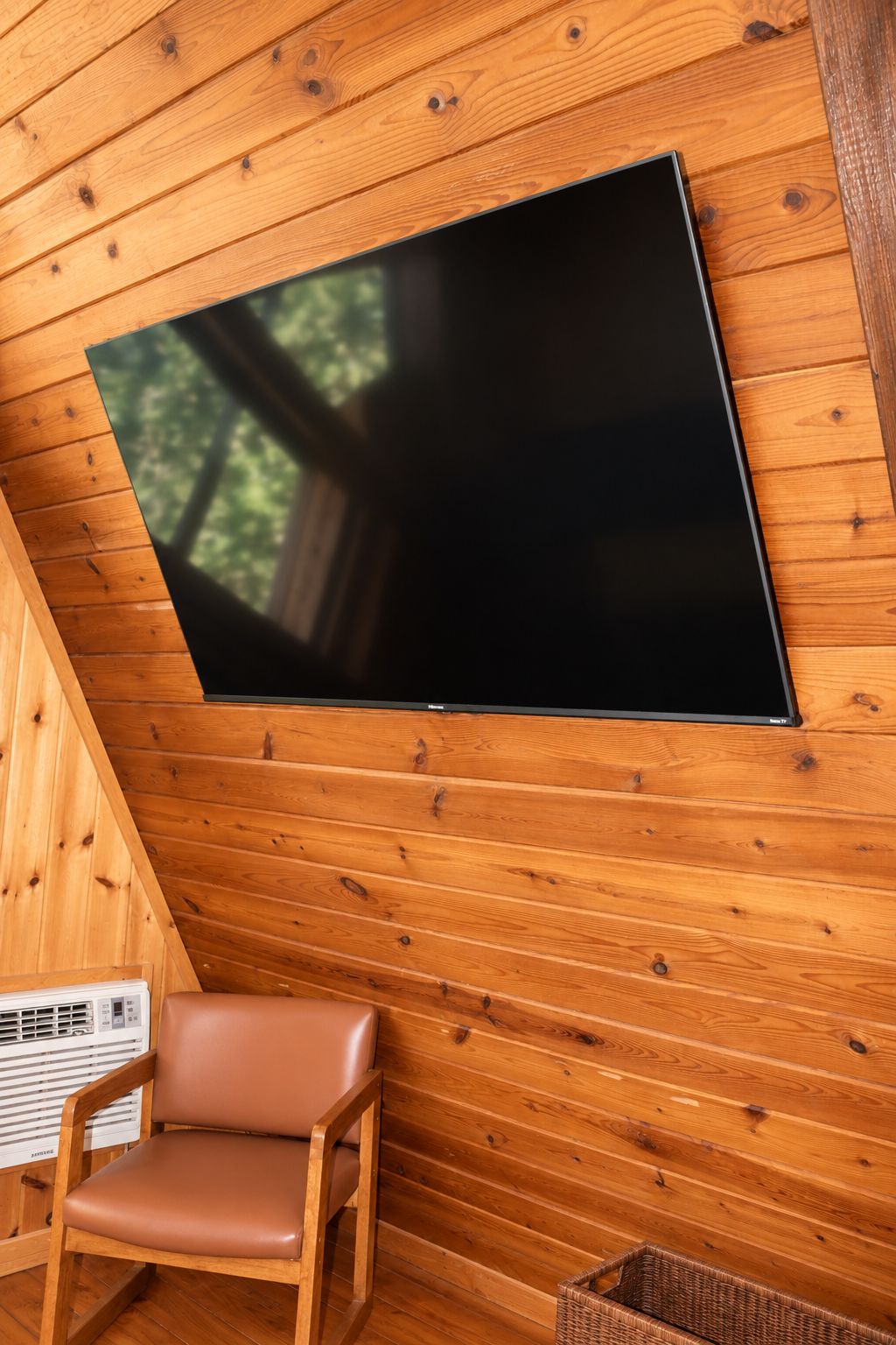 Un interior de madera con un televisor de pantalla plana montado, un sillón de cuero y una cesta de mimbre.