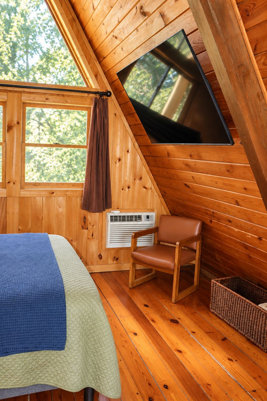 Una habitación cálida tipo cabaña con una cama, un sillón, un televisor y una ventana.
