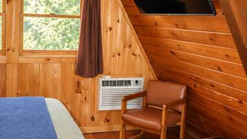 Una habitación cálida tipo cabaña con una cama, un sillón, un televisor y una ventana.