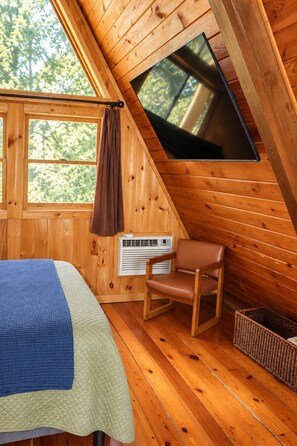 A cozy cabin room with a bed, a chair, a TV, and a window.