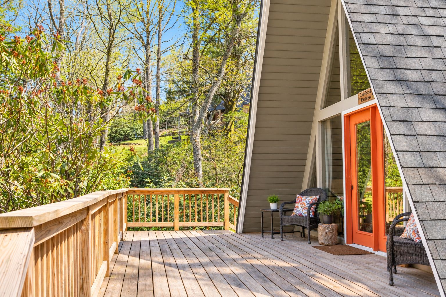 A wooden deck with a railing, a wicker chair, a small table, and a door leading to a covered area.