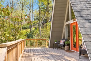 A wooden deck with a railing, a wicker chair, a small table, and a door leading to a covered area.