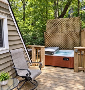 A wooden deck with a hot tub, a chair, and a table with a plant.