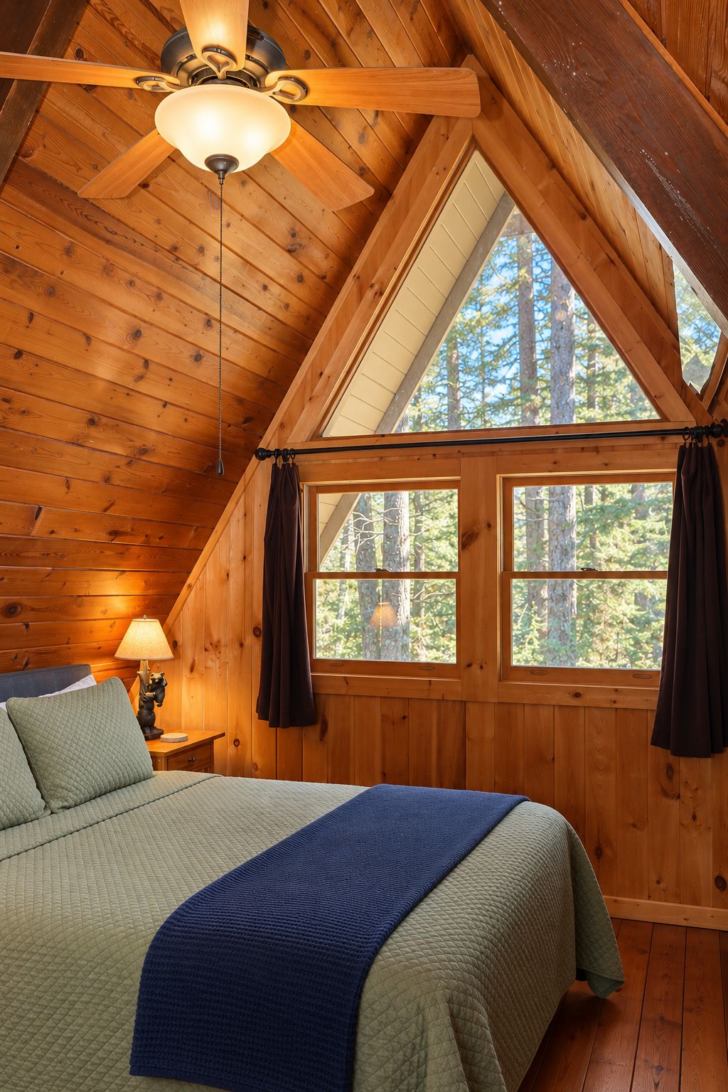 A wooden cabin bedroom with a bed, a nightstand, a lamp, and a ceiling fan.