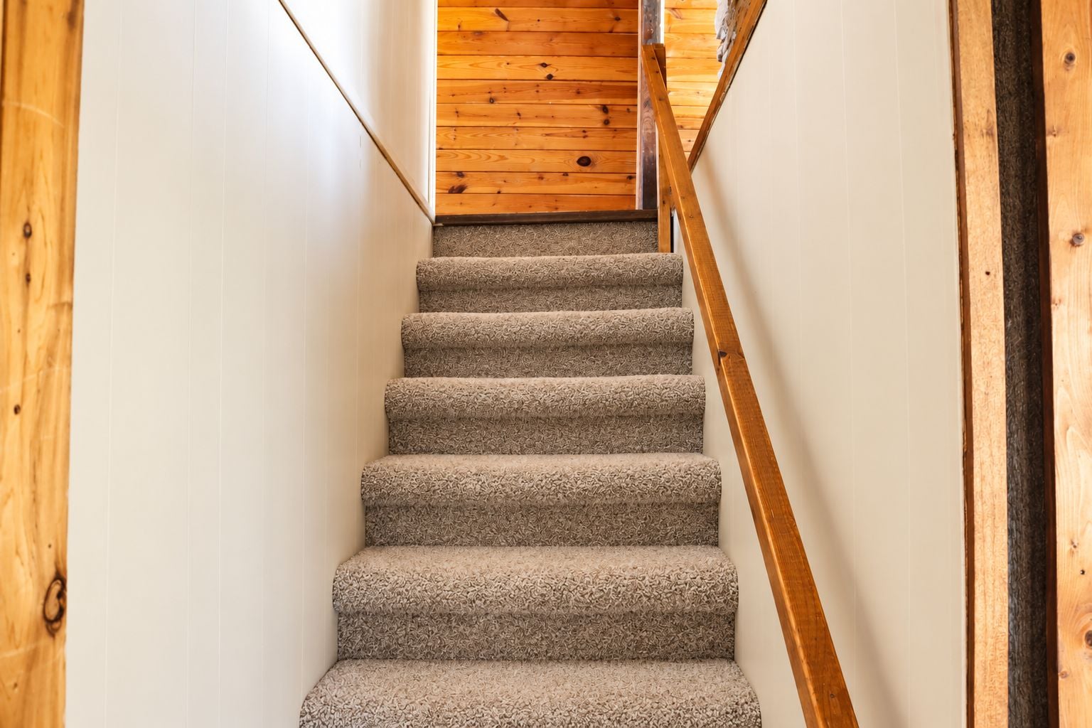 A carpeted staircase with wooden handrails, leading to a wooden floor.