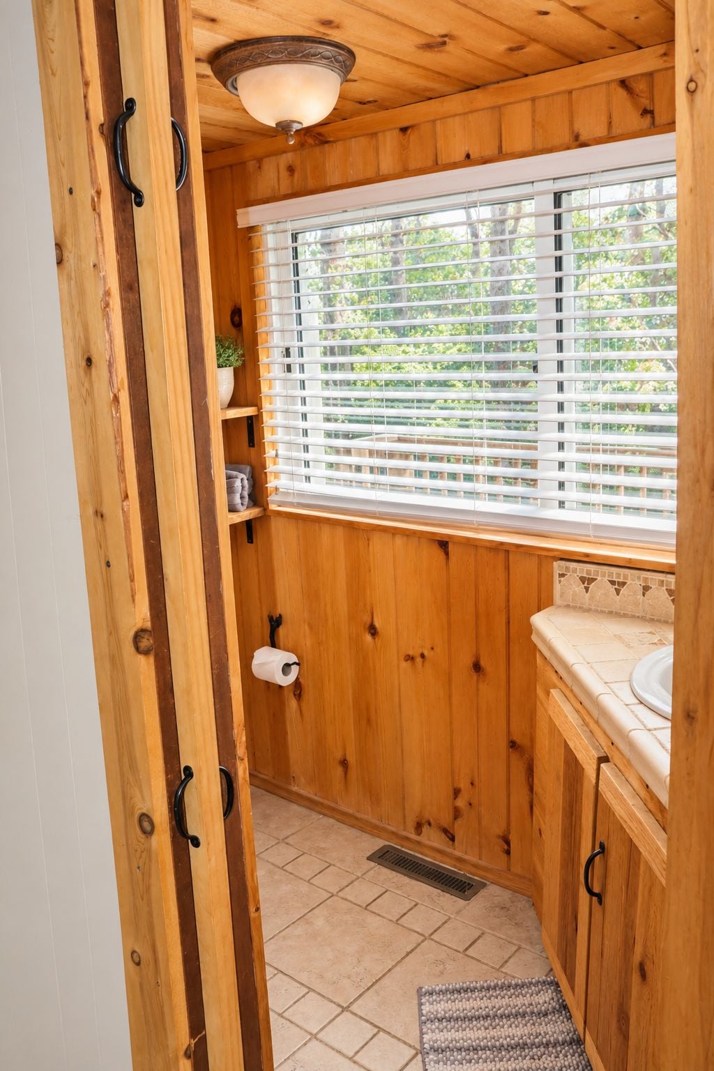 A wooden bathroom with a window, toilet paper, and a sink.
