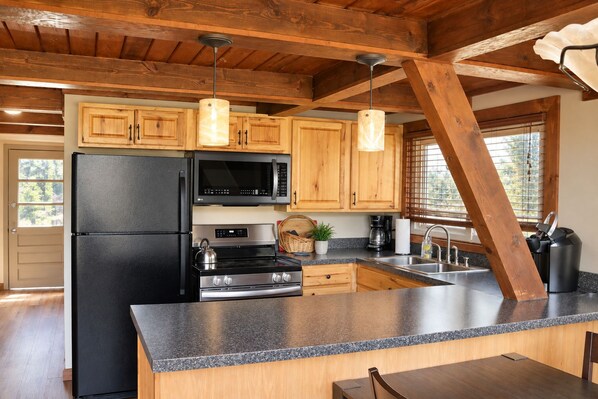 A kitchen with wooden cabinets, a black refrigerator, a microwave, a stove, and a granite countertop.