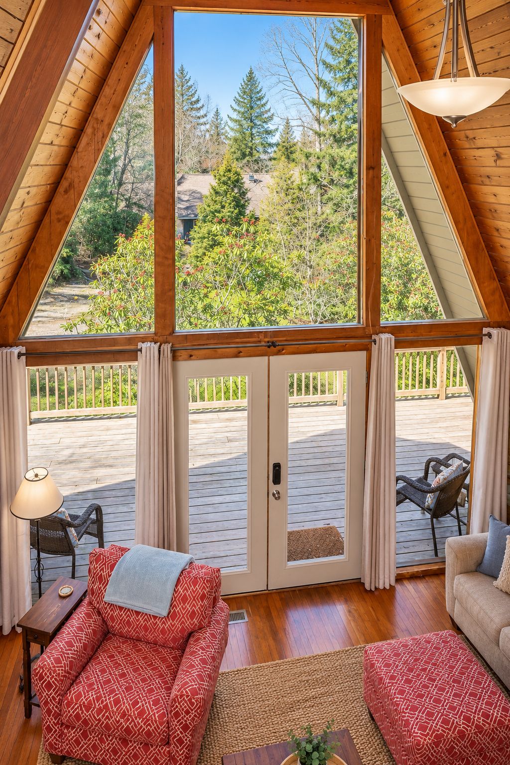 A cozy interior with a wooden ceiling, a large window, and a view of a deck and trees.