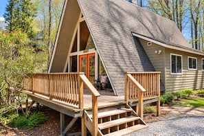 En hytte med et stejlt tag, en træterrasse med trapper og en dør med teksten 'Cottage'.