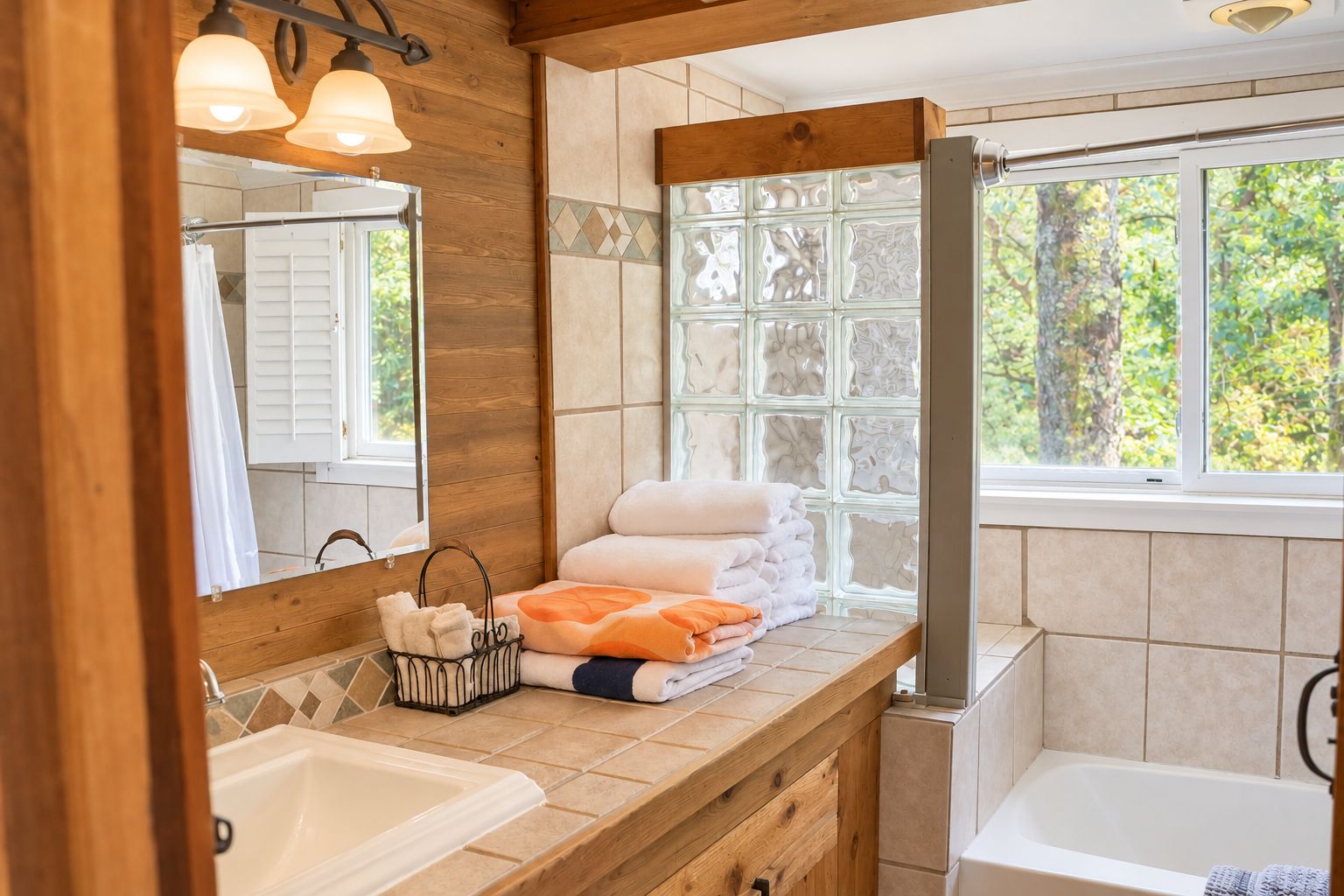 Ein Badezimmer mit einem Holzkosmetikschrank, einem großen Spiegel, einer Badewanne und einem Fenster mit Blick auf Bäume.