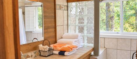 Ein Badezimmer mit einem Holzkosmetikschrank, einem großen Spiegel, einer Badewanne und einem Fenster mit Blick auf Bäume.