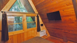 Une cabane triangulaire en bois, dotée d’une grande fenêtre et d’un petit panneau noir sur le mur.