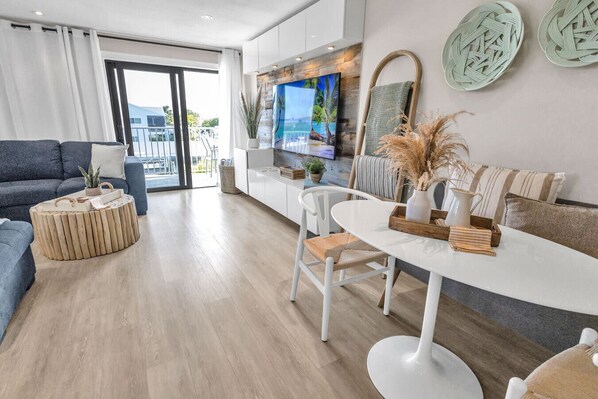 A modern living room with a sofa, a round coffee table, a dining table with chairs, and a TV mounted on a wooden wall. - Key Largo Ocean Shore Villa 1 with pool & boat slip (Key Largo)