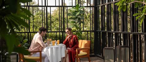 A couple dining at an outdoor table with a view of greenery and a metal fence.