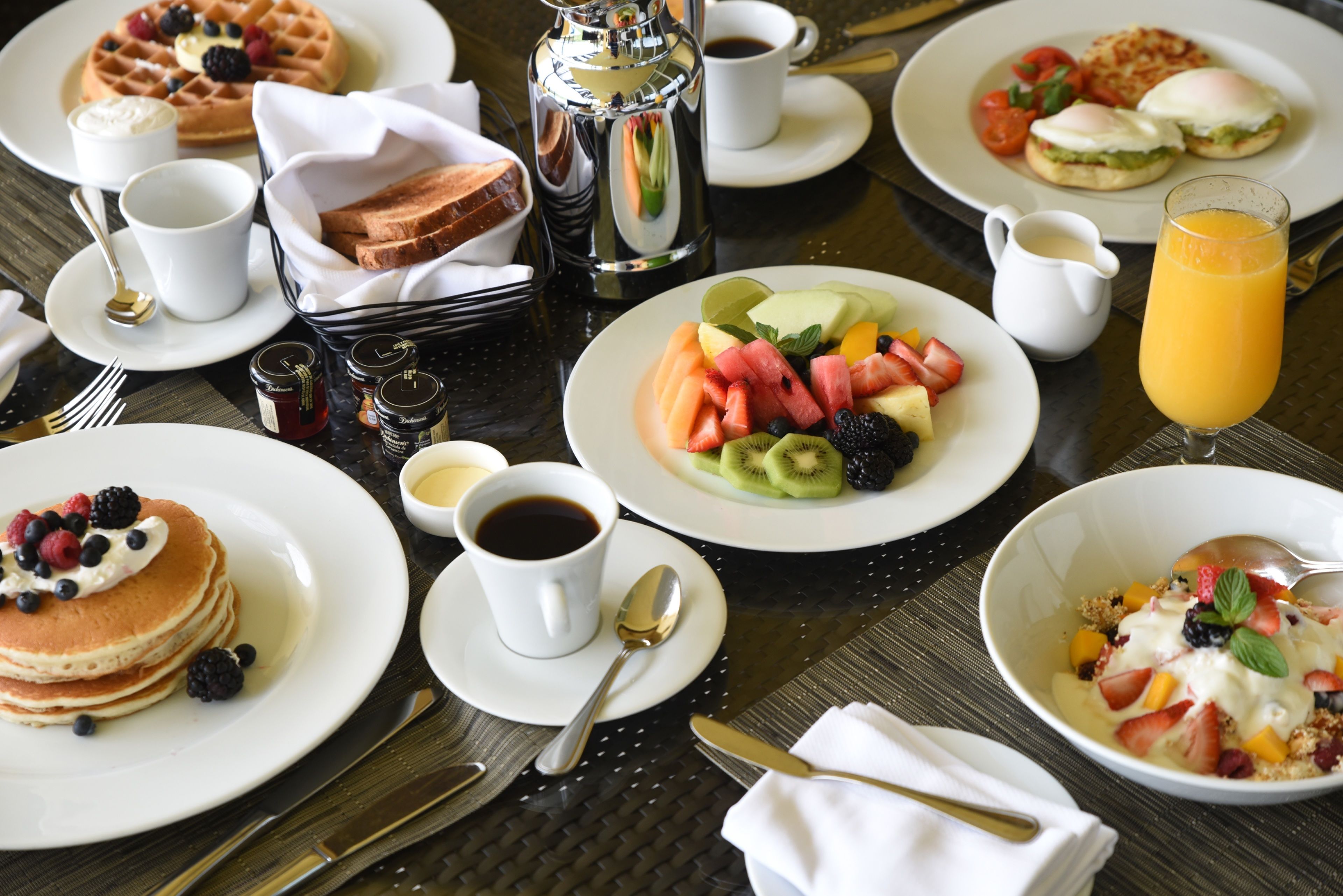 Buffet de café da manhã com diversos pratos, incluindo panquecas, waffles e saladas de frutas.