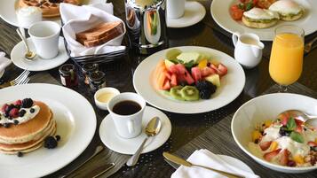 Buffet de café da manhã com diversos pratos, incluindo panquecas, waffles e saladas de frutas.
