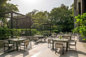 Un patio al aire libre con varias mesas y sillas, rodeado de follaje y árboles.