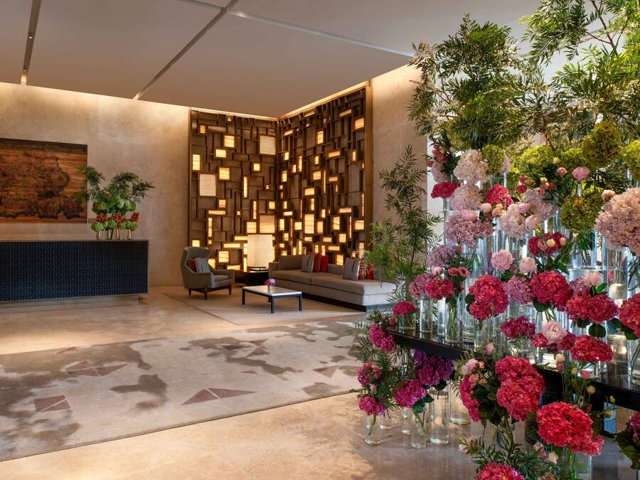 En lobby med et moderne design, med en sektionsvæg med geometriske mønstre, en sofa, et sofabord og en blomsterdekoration.