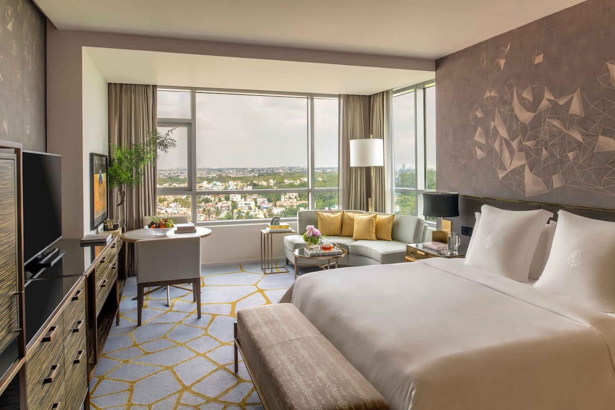 A modern hotel room with a large bed, a desk, a sofa, and a view of the city.