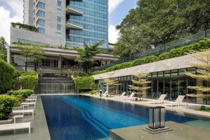 Un hotel moderno con piscina, sillas de descanso y un edificio de fachada de vidrio al fondo.