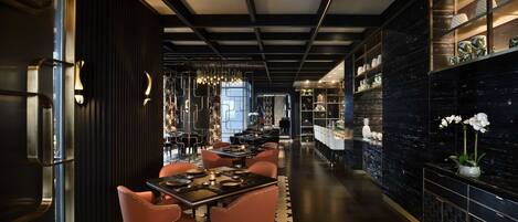 A modern restaurant interior with black and white decor, a long dining area, and a bar with shelves of decorative items.
