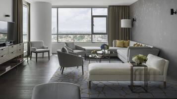 Una habitación de hotel moderna con un ventanal grande, un sofá, una silla, una mesita de café y un televisor.
