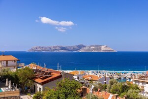 Vista costera con un puerto deportivo, edificios con techos de tejas rojas y una isla distante.