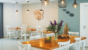 A dining area with wooden tables and white chairs, a brick wall, and hanging pendant lights. - Luvi Kaş Otel - Adults Only (Kas)