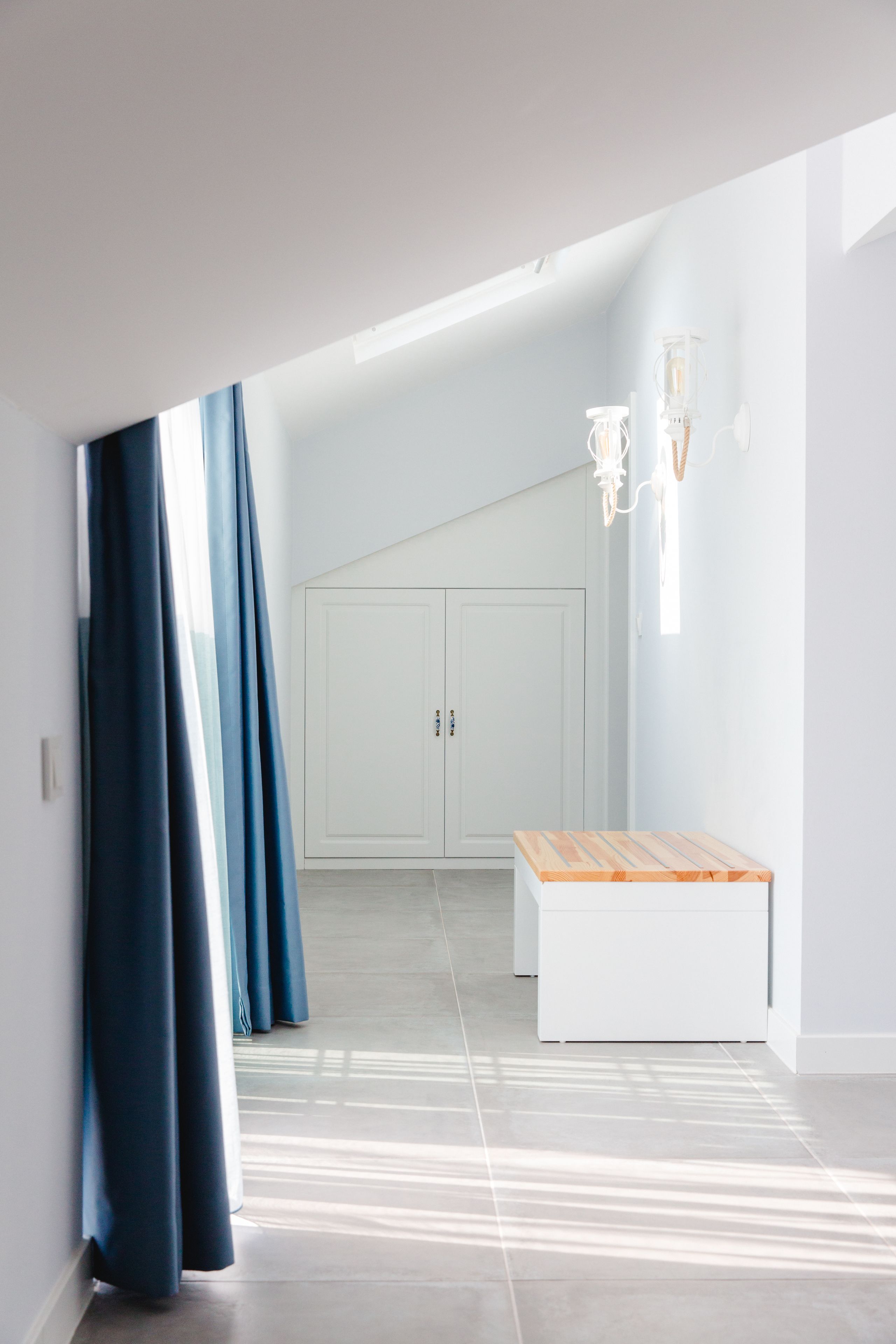 A modern hallway with a sloped ceiling, a white bench, and a door in the background.