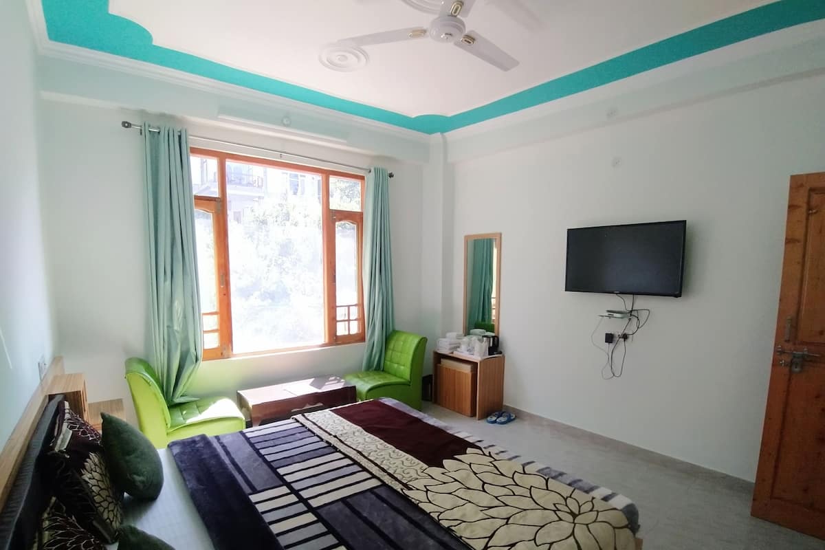 Quarto com cama, escrivaninha, cadeira, televisão e janela com cortinas.