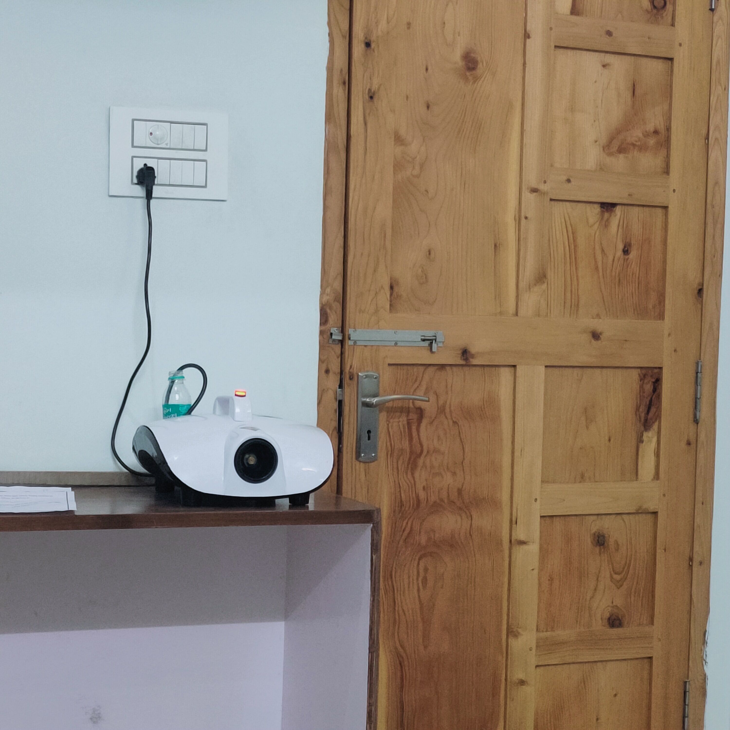 A projector on a desk with a wooden door and a power outlet in the background.