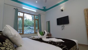 A hotel room with a large bed, a flat-screen TV mounted on the wall, and a window with curtains. - Hotel Sarla Regency (Bhuntar)