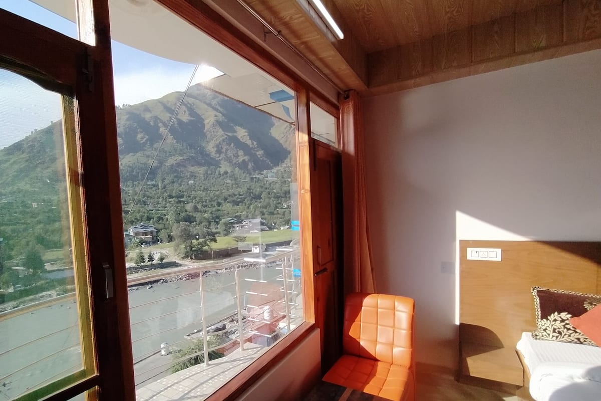 Quarto com uma grande janela que oferece vista para uma paisagem montanhosa e uma estrada.