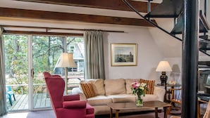 A living room with a sofa, armchair, coffee table, and a painting on the wall. - Cottages at the Even'tide Resort (Wellfleet)