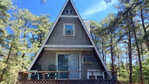A triangular A-frame cabin with a porch, surrounded by trees. - Cottages at the Even'tide Resort (Wellfleet)