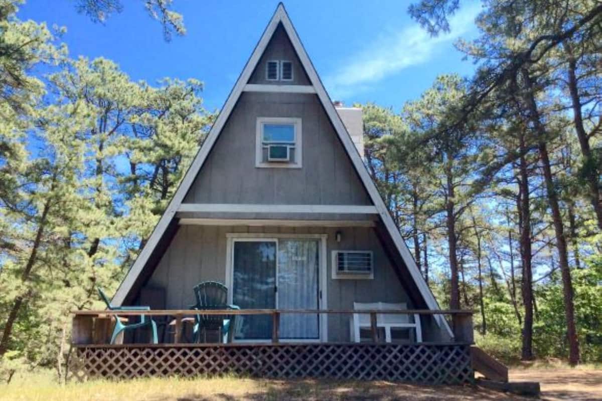 A triangular A-frame cabin with a porch, surrounded by trees.
