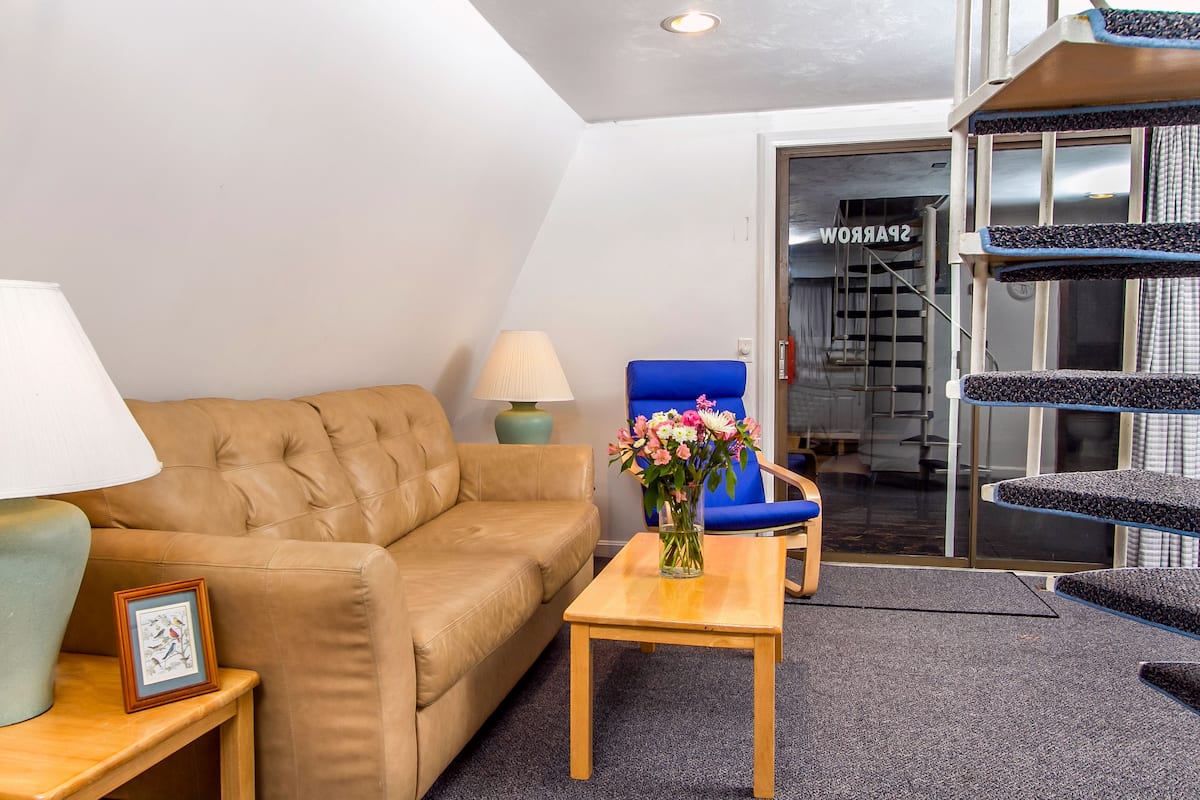 A living room with a sofa, a table with a vase of flowers, a lamp, and a chair.