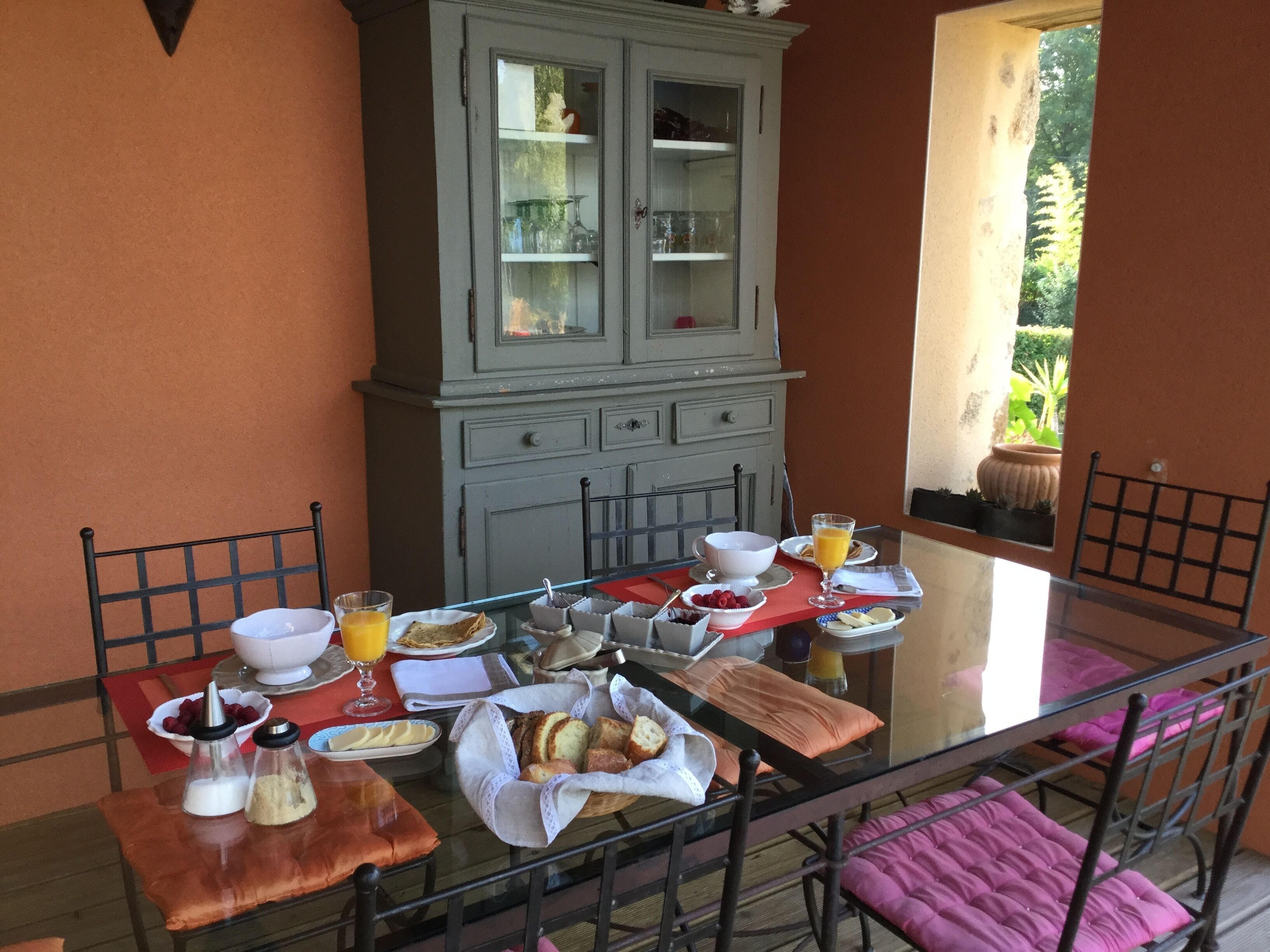 Una mesa de desayuno dispuesta con diferentes platos, incluyendo un bol de fruta, un vaso de zumo de naranja y pan.