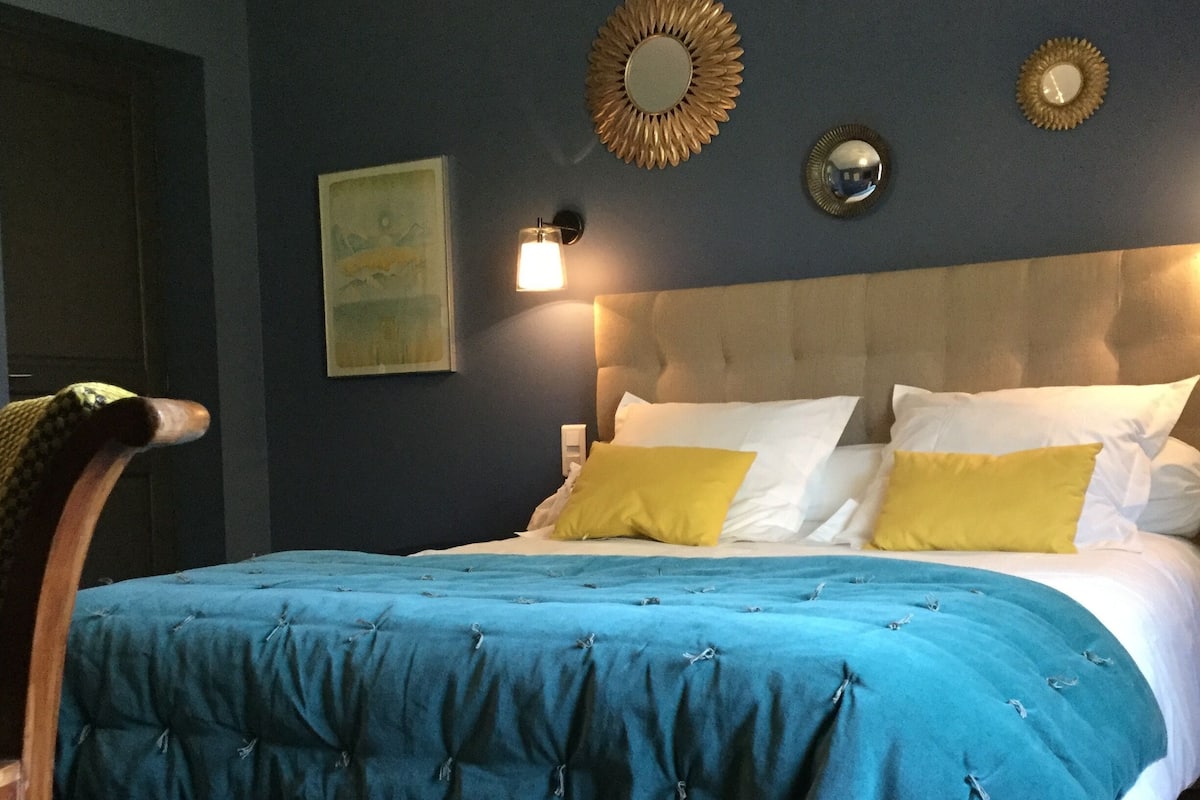 A bedroom with a tufted headboard, a blue bedspread, and two yellow pillows.