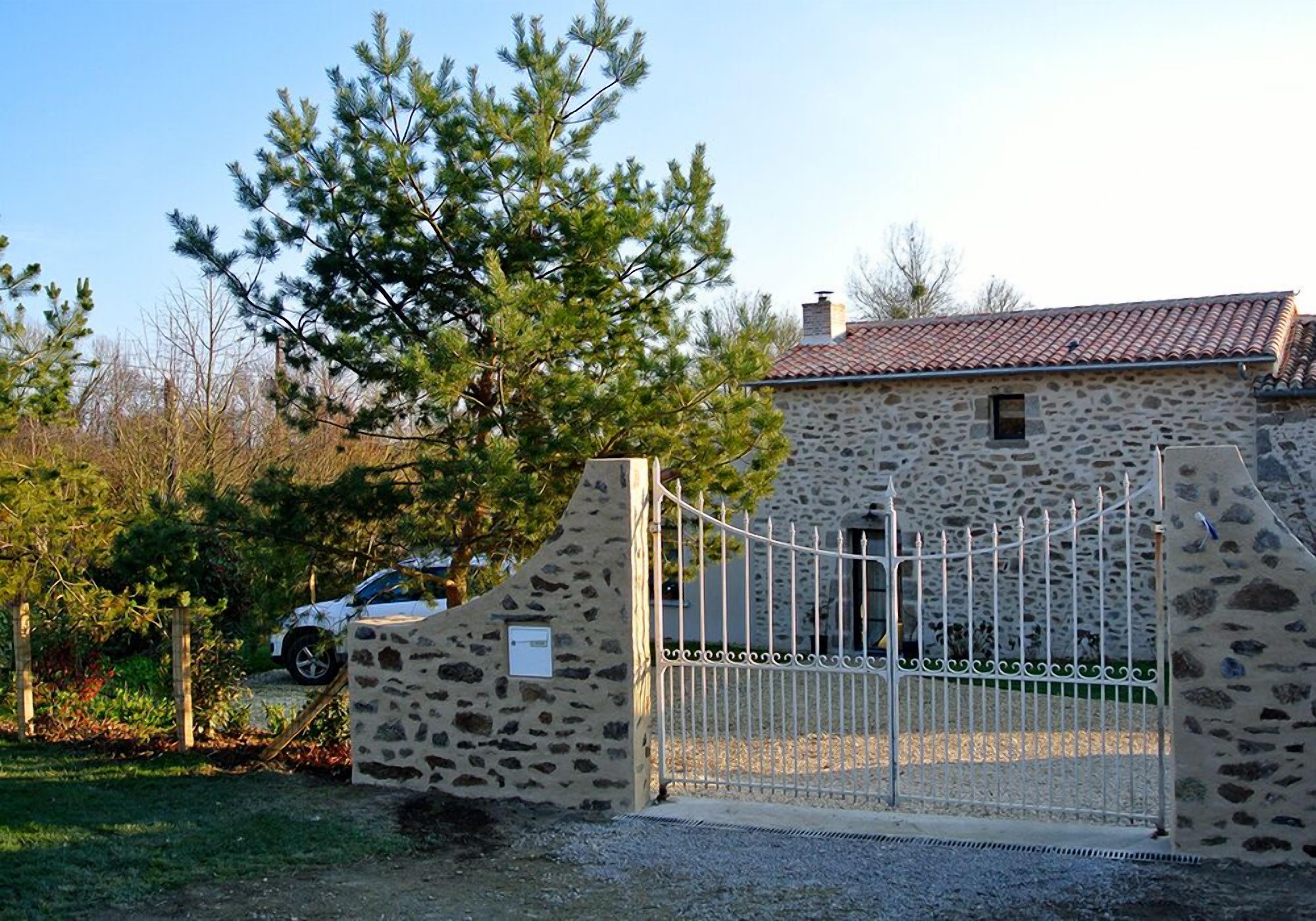 A stone building with a metal gate, a parked car, and a tree in the background.