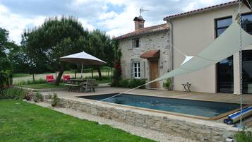 A swimming pool with a stone deck, a patio with outdoor furniture, and a house with a stone facade and tiled roof.