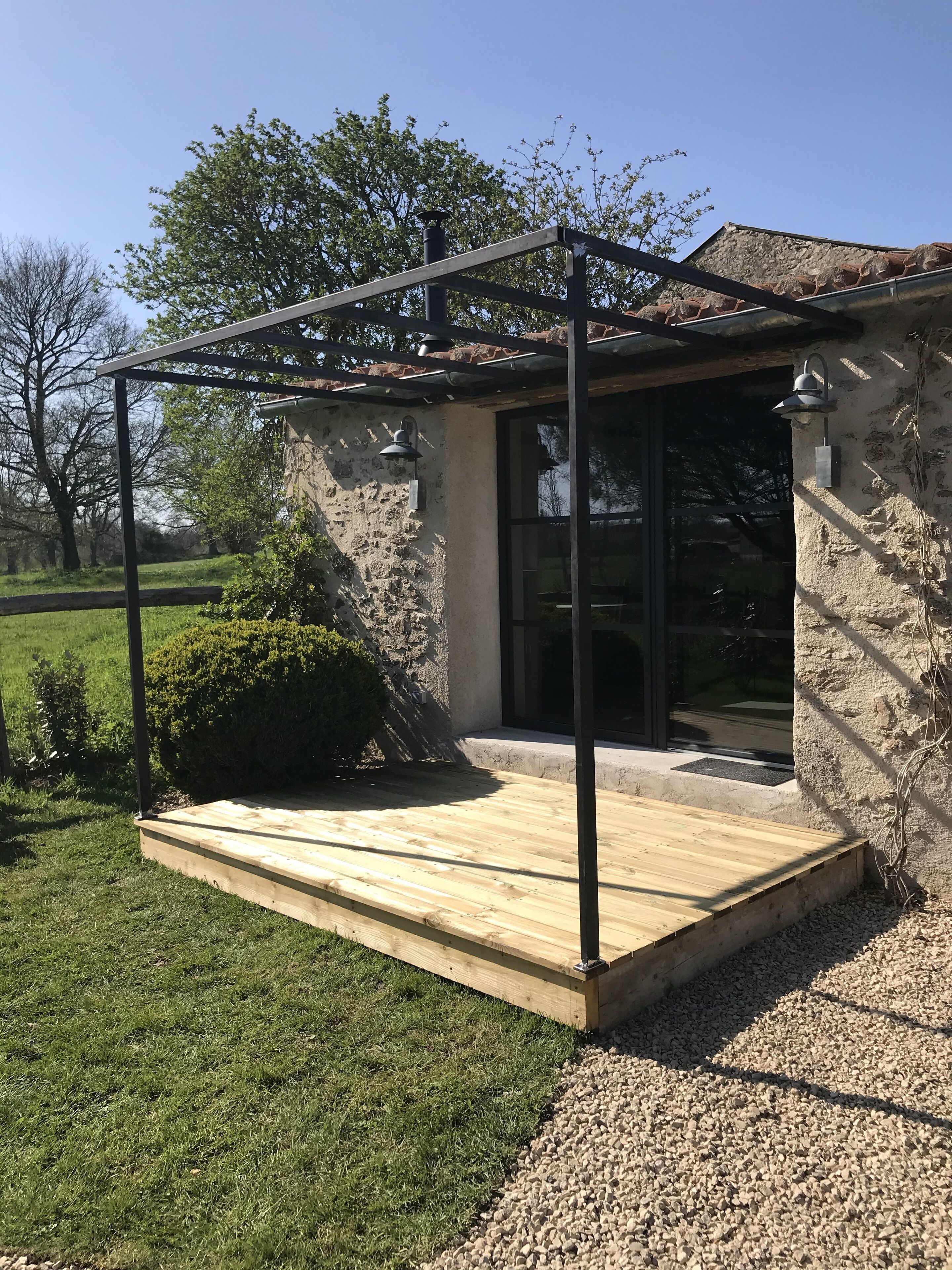 A covered patio area with a wooden deck, stone walls, and a pergola structure.