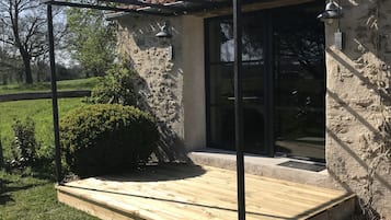 A covered patio area with a wooden deck, stone walls, and a pergola structure.