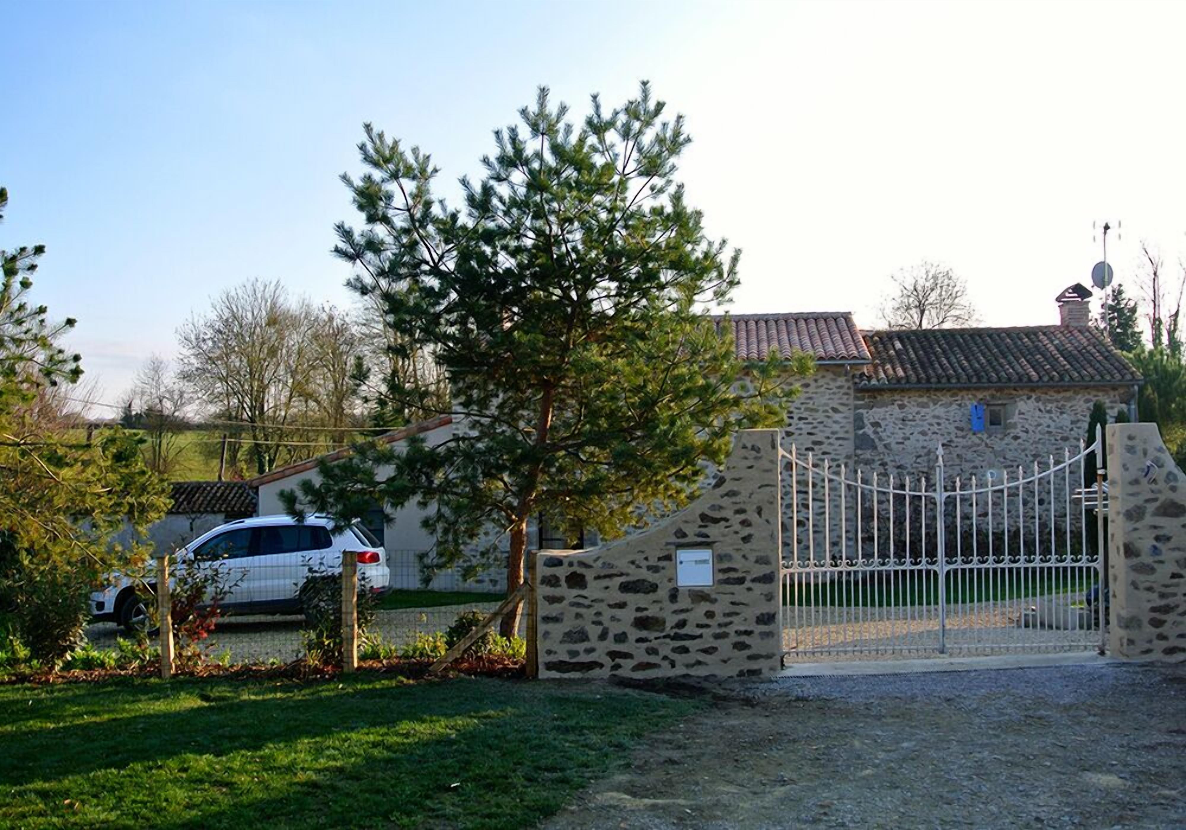 A stone building with a metal gate, a parked car, and a tree in front.