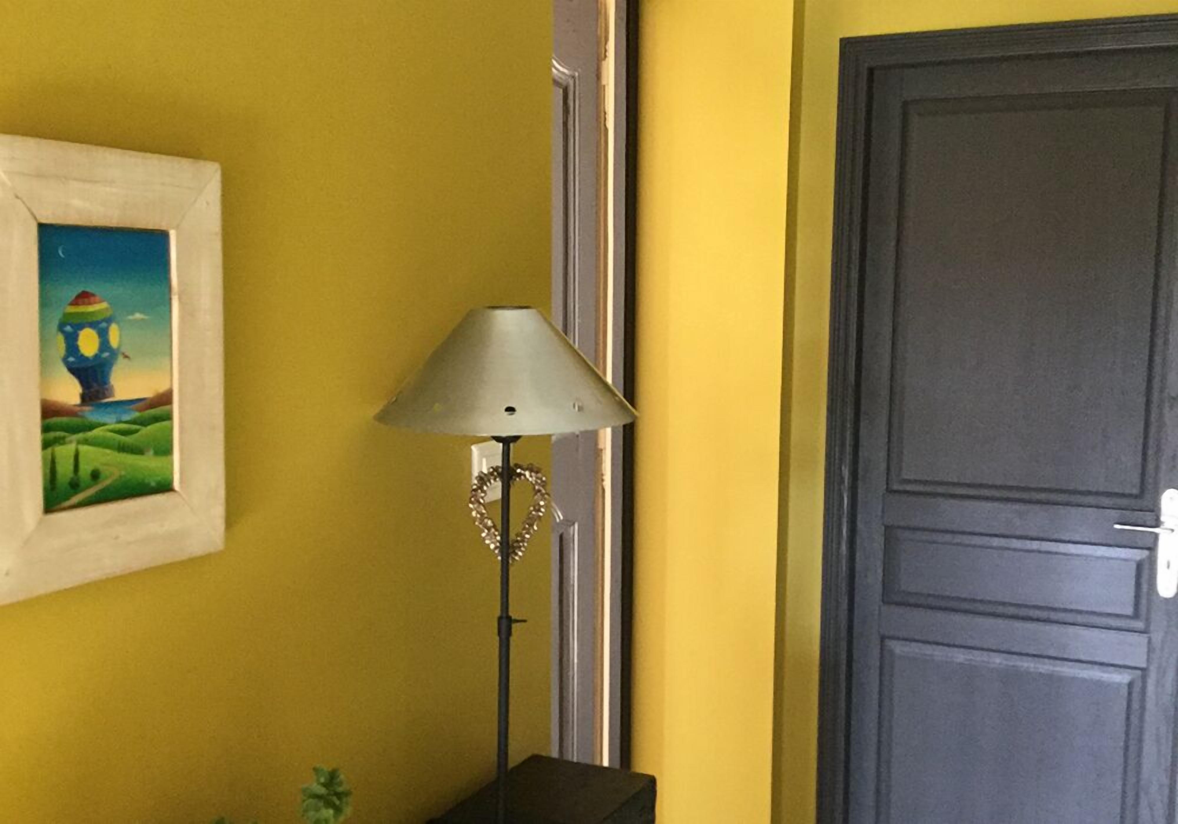 A room with a yellow wall, a framed picture, a floor lamp, and a door.