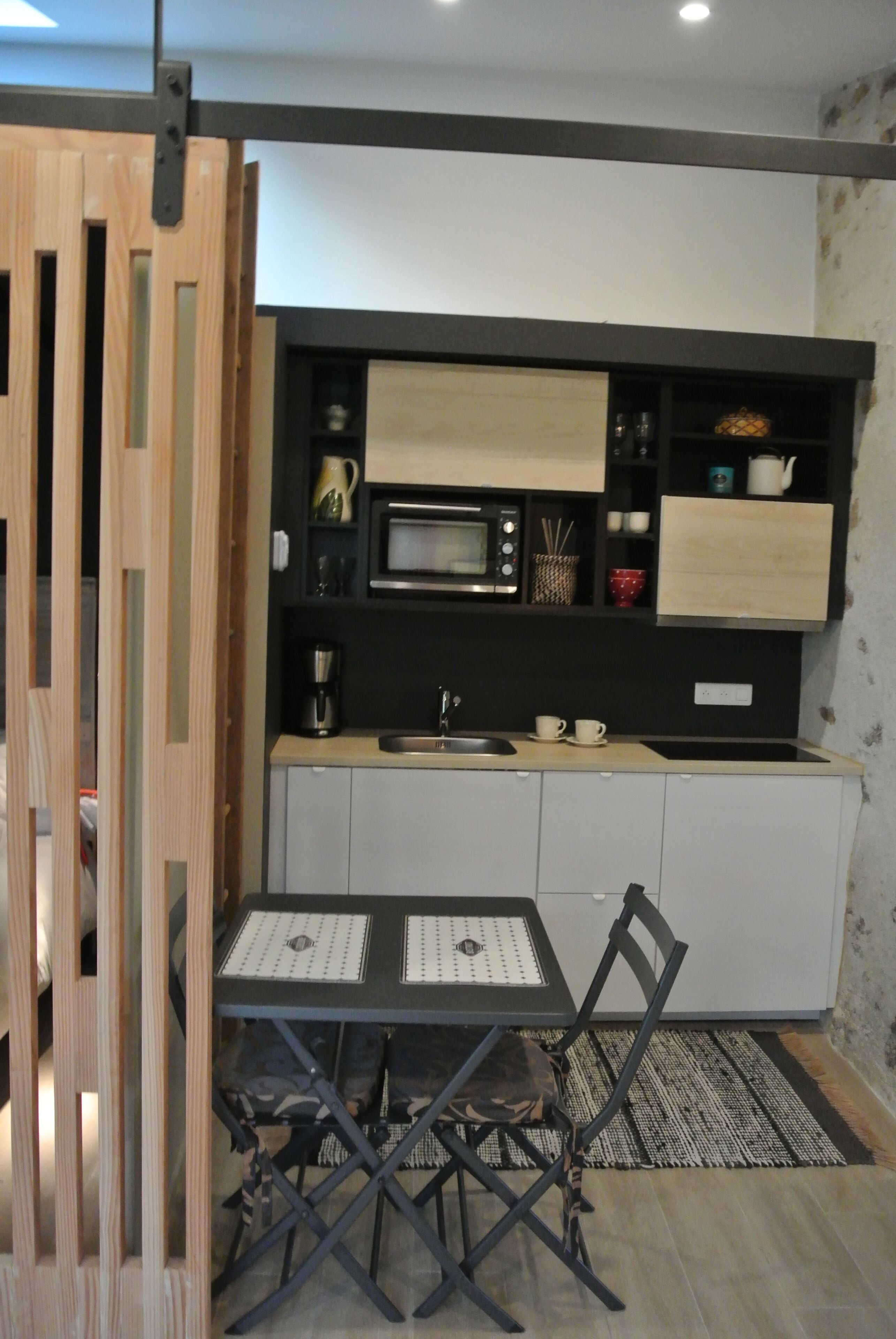 Uma cozinha compacta com micro-ondas, cafeteira e um pequeno espaço de refeições com mesa e cadeiras.