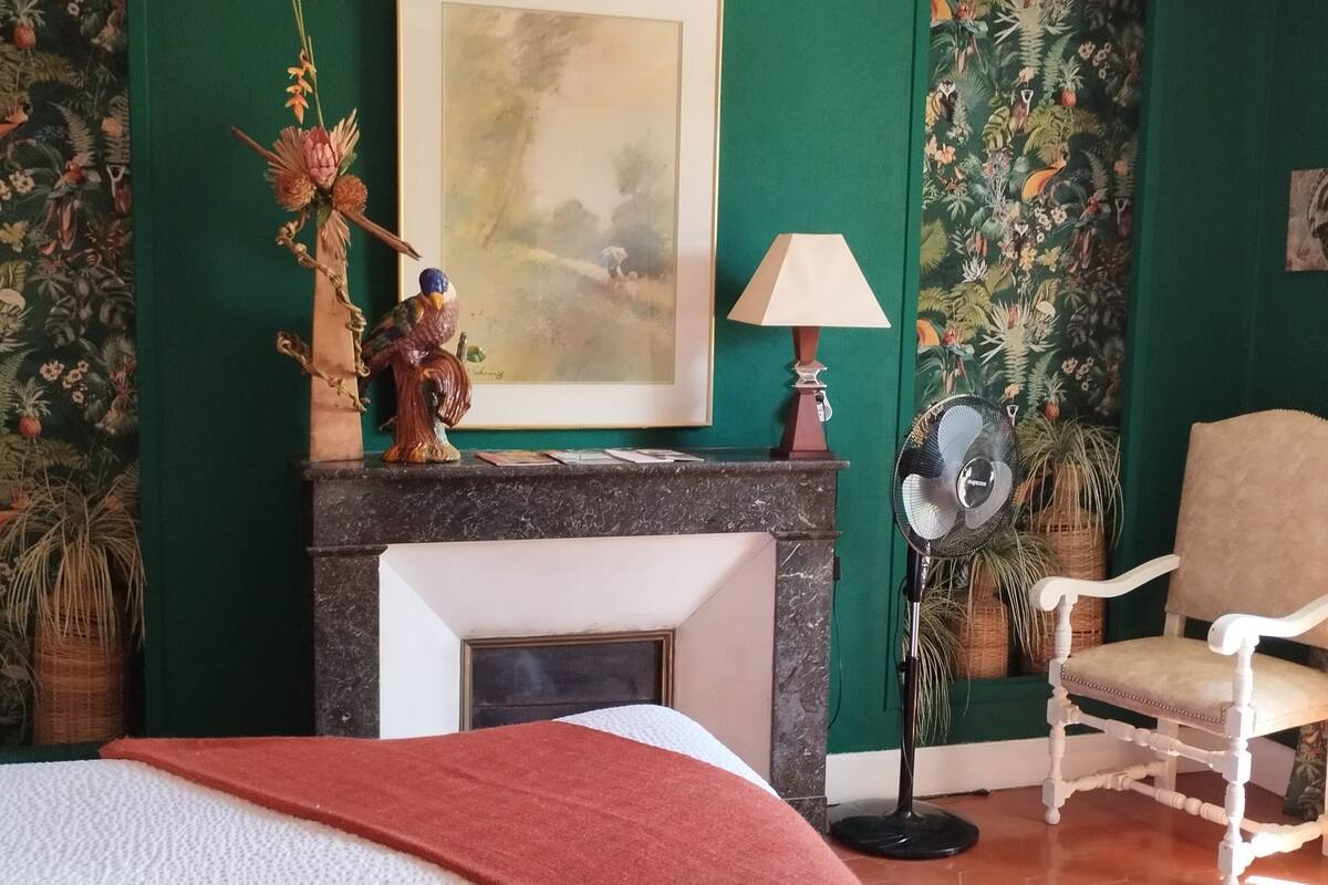 A bedroom with a bed, a fireplace, a chair, and a fan.